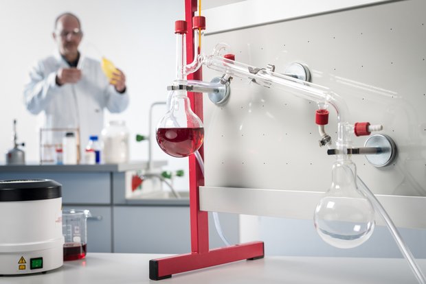 Lehrkraft führt ein Demonstrationsexperiment zum Thema Destillation in der Organischen Chemie durch. Der Versuch ist am Chemie-Präsenations-System aufgebaut.